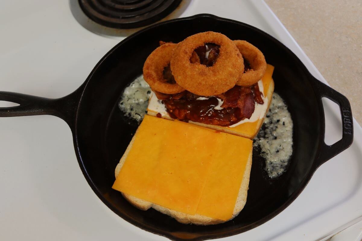 Onion rings stacked over barbecue chicken, bacon and cheese on bread in a skillet.