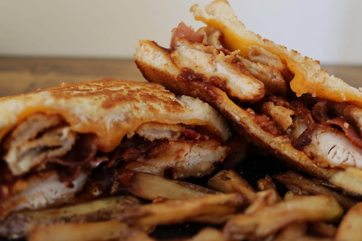 Grilled chicken and bacon sandwich cut in half with fries.