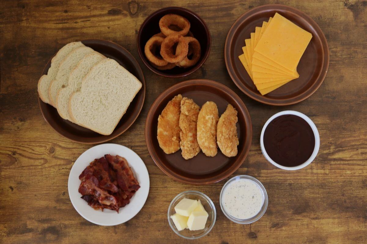 Sliced bread, chicken tenders, bacon, cheese, onion rings, sauce, and butter on plates.
