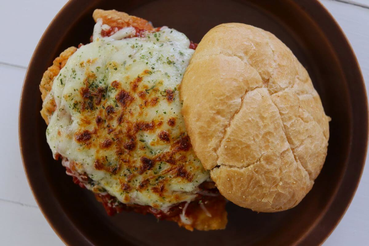 Chicken sandwich with melted cheese and marinara sauce on a roll on a brown plate.