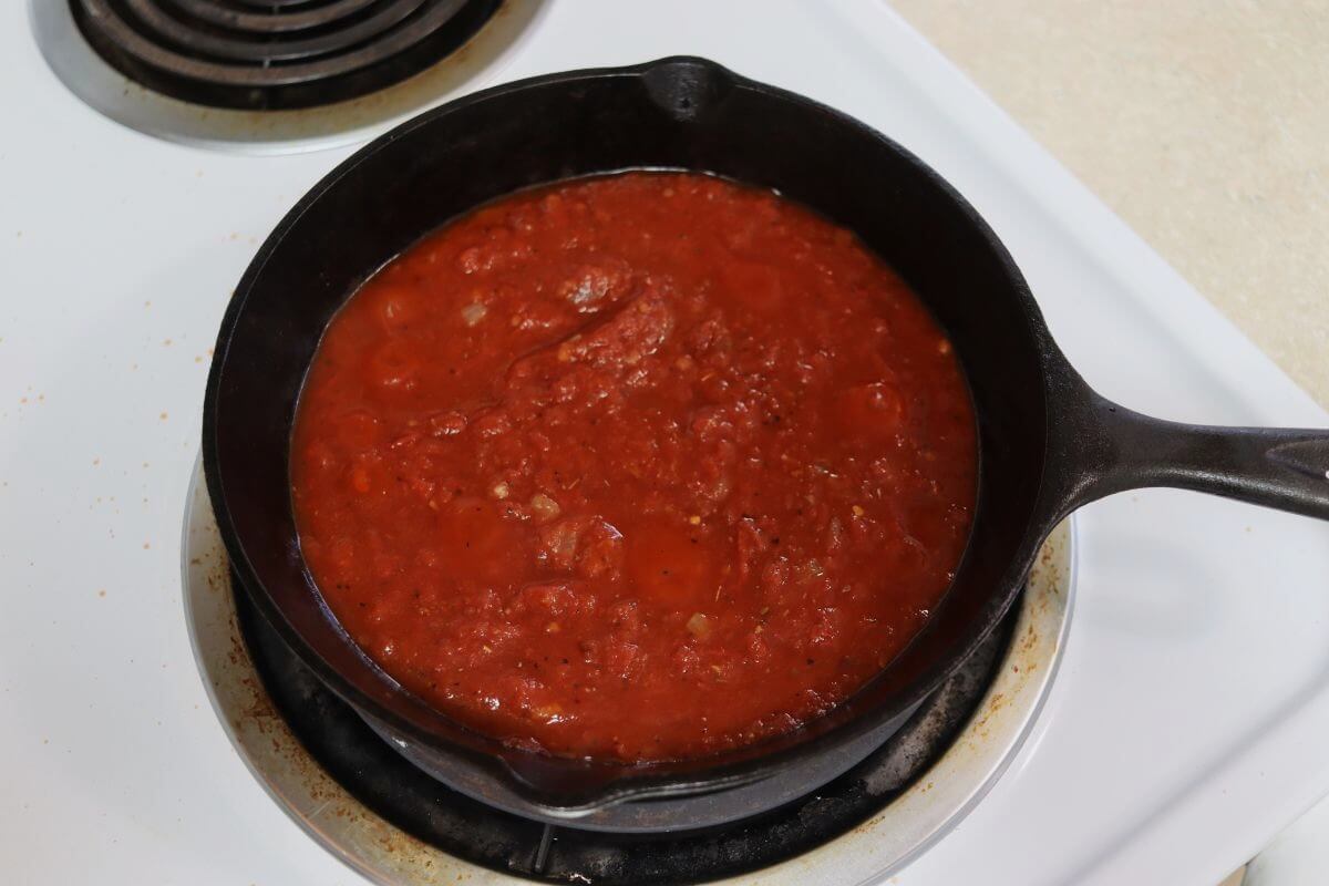 Tomato sauce simmering in a cast iron skillet on a stovetop burner.
