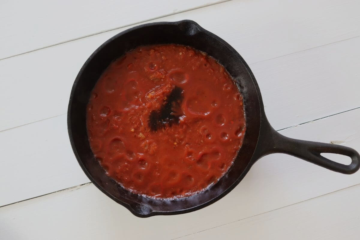 Tomato sauce in cast iron skillet with balsamic vinegar added on white surface.