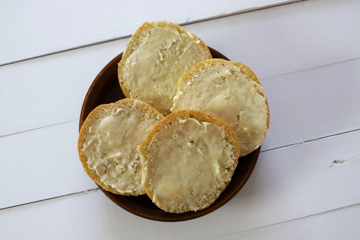 Four sandwich roll halves spread with butter on a brown plate.