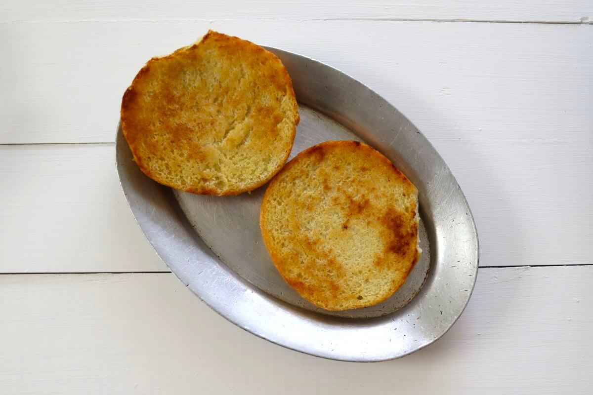 Two toasted sandwich roll halves on a metal pan.