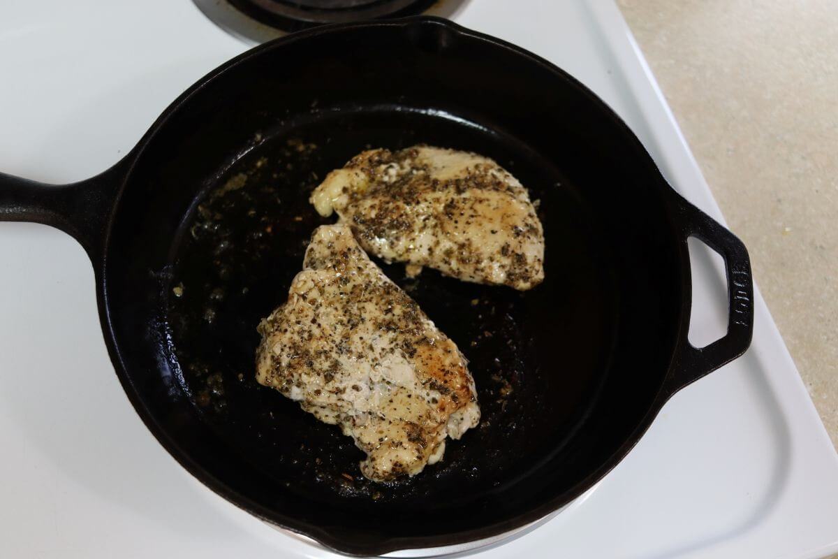 Seasoned chicken breasts cooking in a cast iron skillet on a stovetop.