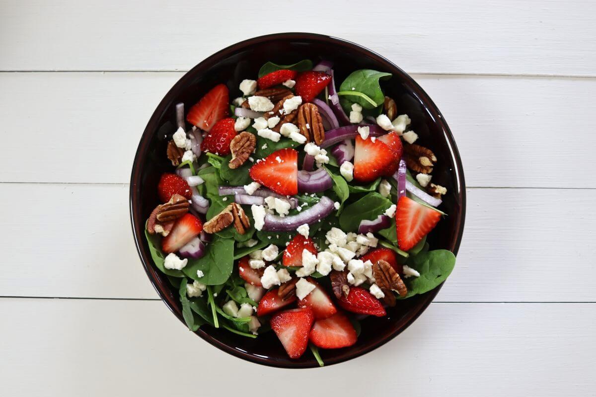 Spinach salad topped with sliced strawberries, red onion, pecans, and crumbled feta cheese in a bowl.