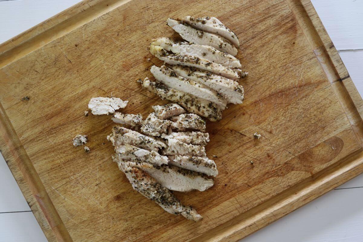 Sliced seasoned chicken breast cut into strips on a wooden cutting board.