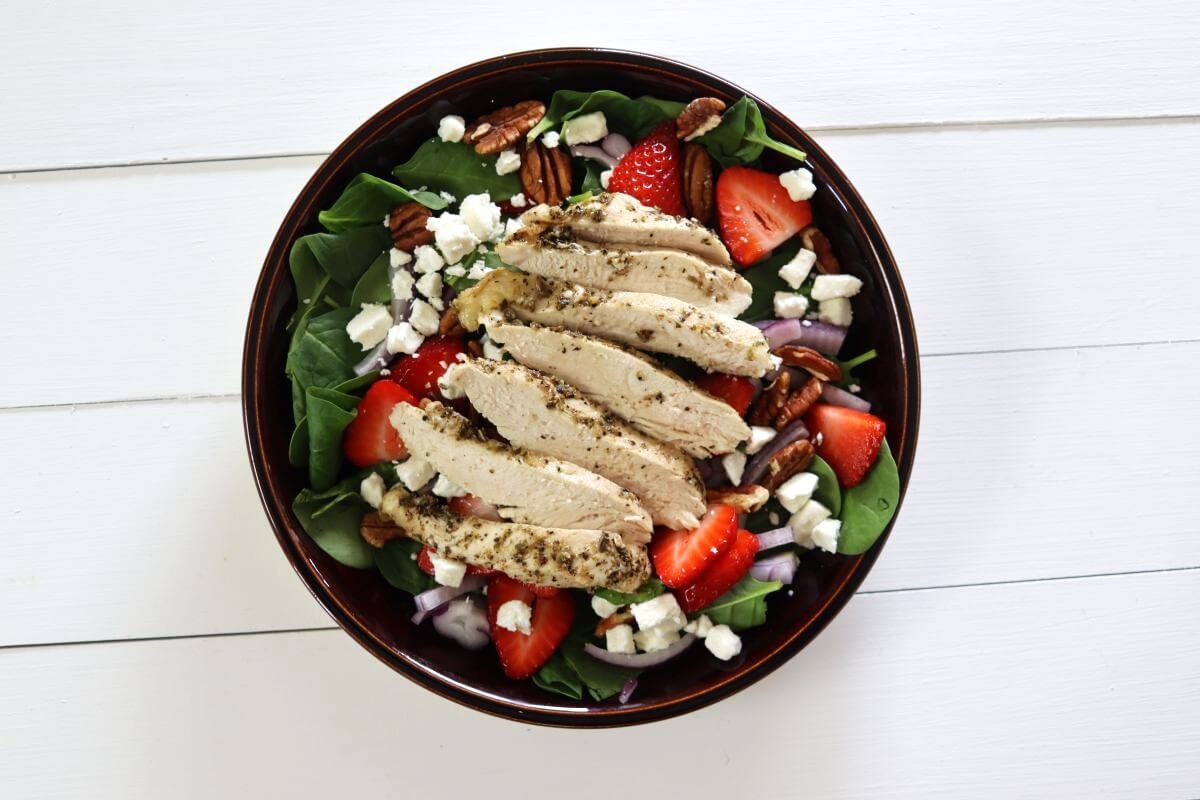 Spinach salad topped with sliced chicken breast, strawberries, pecans, red onion, and feta.