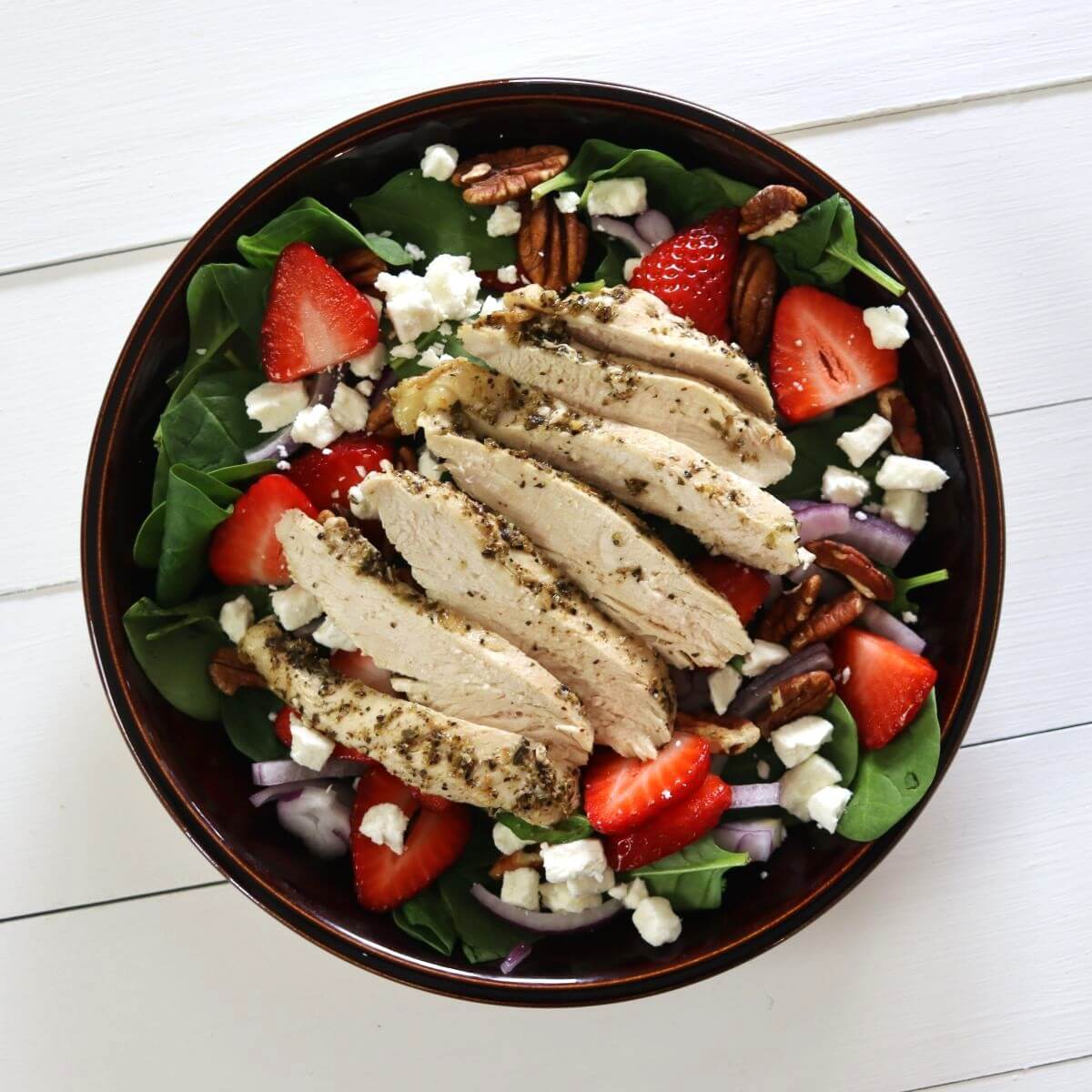 Grilled chicken slices on spinach with strawberries, pecans, red onion, and feta cheese.