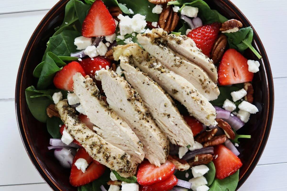 Sliced chicken breast over spinach salad with strawberries, pecans, red onion, and feta cheese.