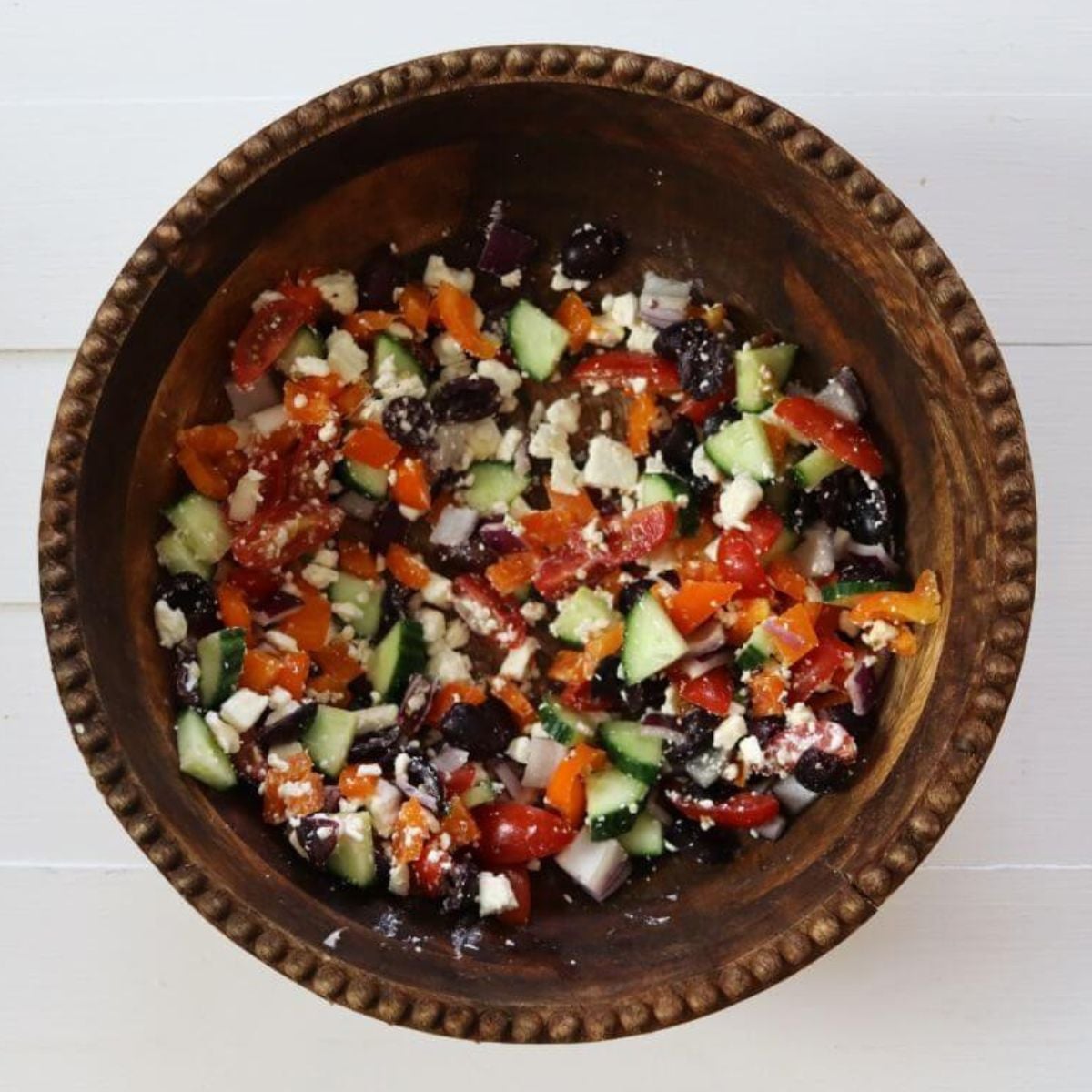 Chopped vegetables, olives, and feta cheese mixed in a wooden bowl.
