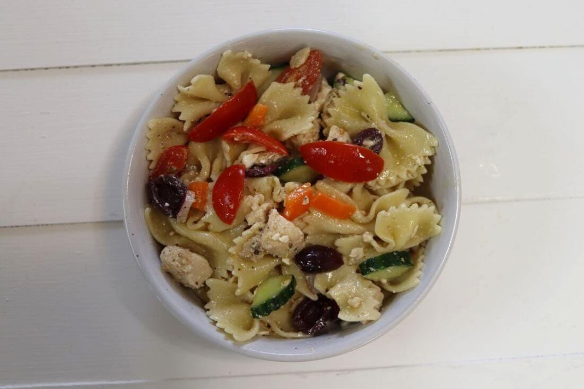 Small bowl of farfalle pasta salad with chicken, tomatoes, cucumber, olives, and feta.