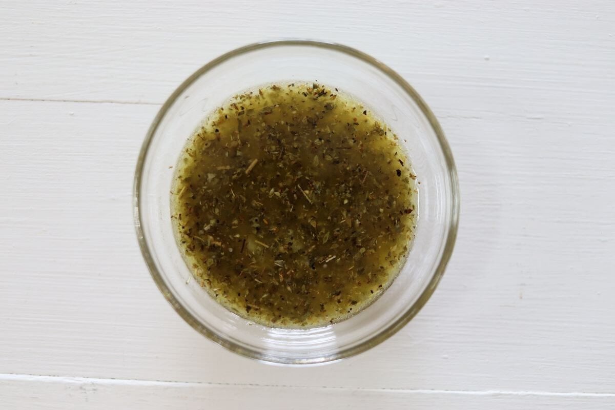 Small glass bowl with olive oil, lemon juice, garlic, and dried herbs mixture.