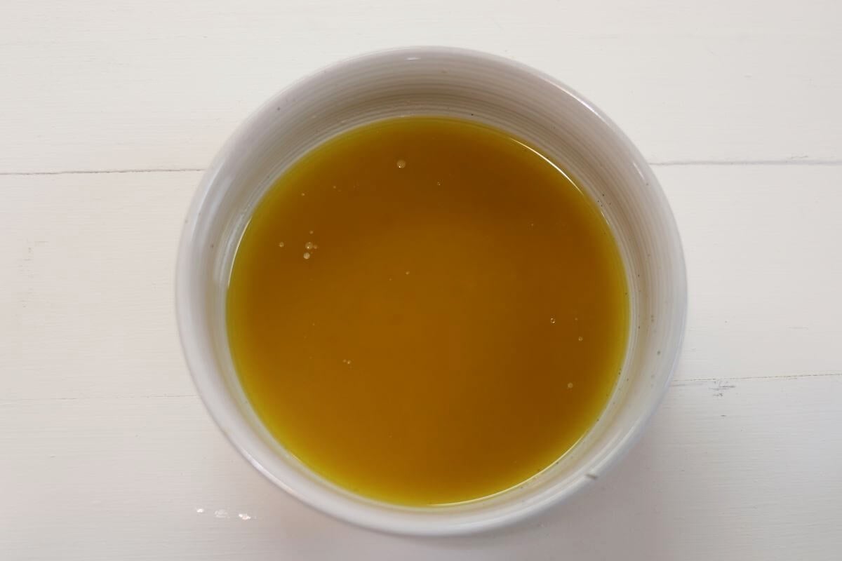 Small white bowl filled with oil and vinegar mixture on a white surface.