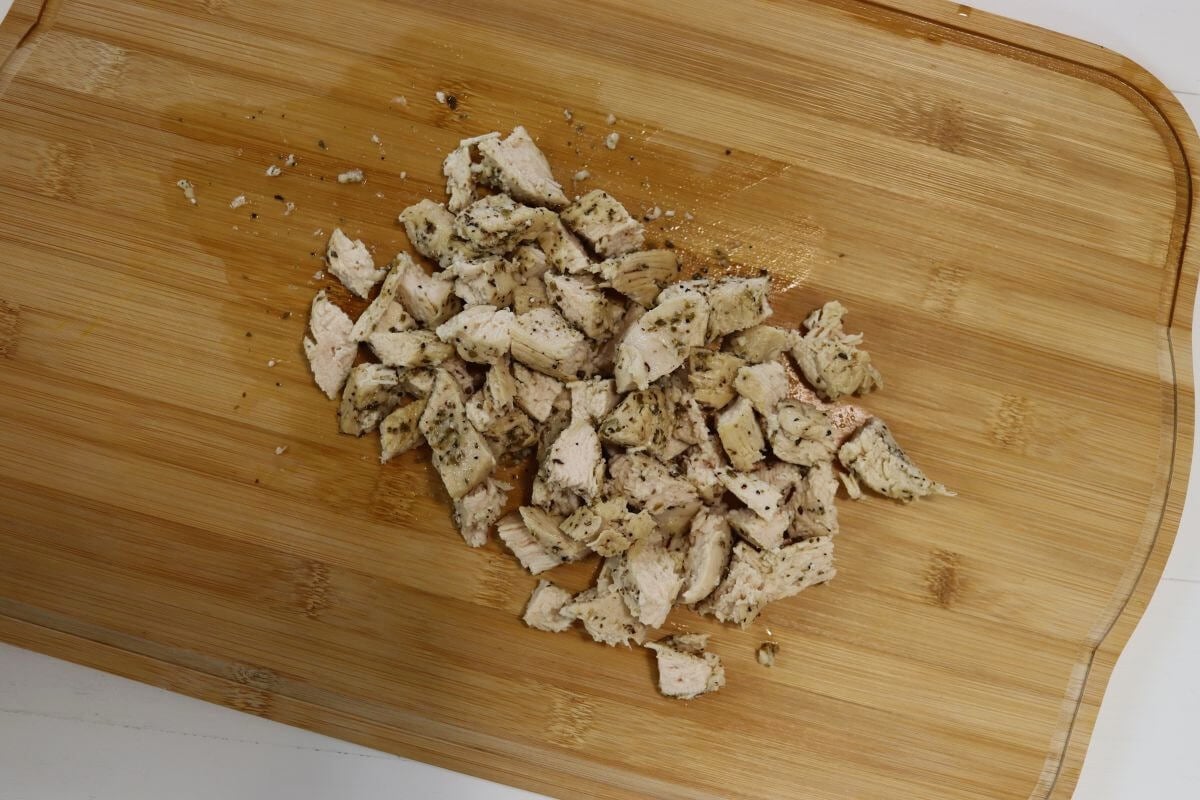 Cooked chicken cut into small pieces on a wooden cutting board.