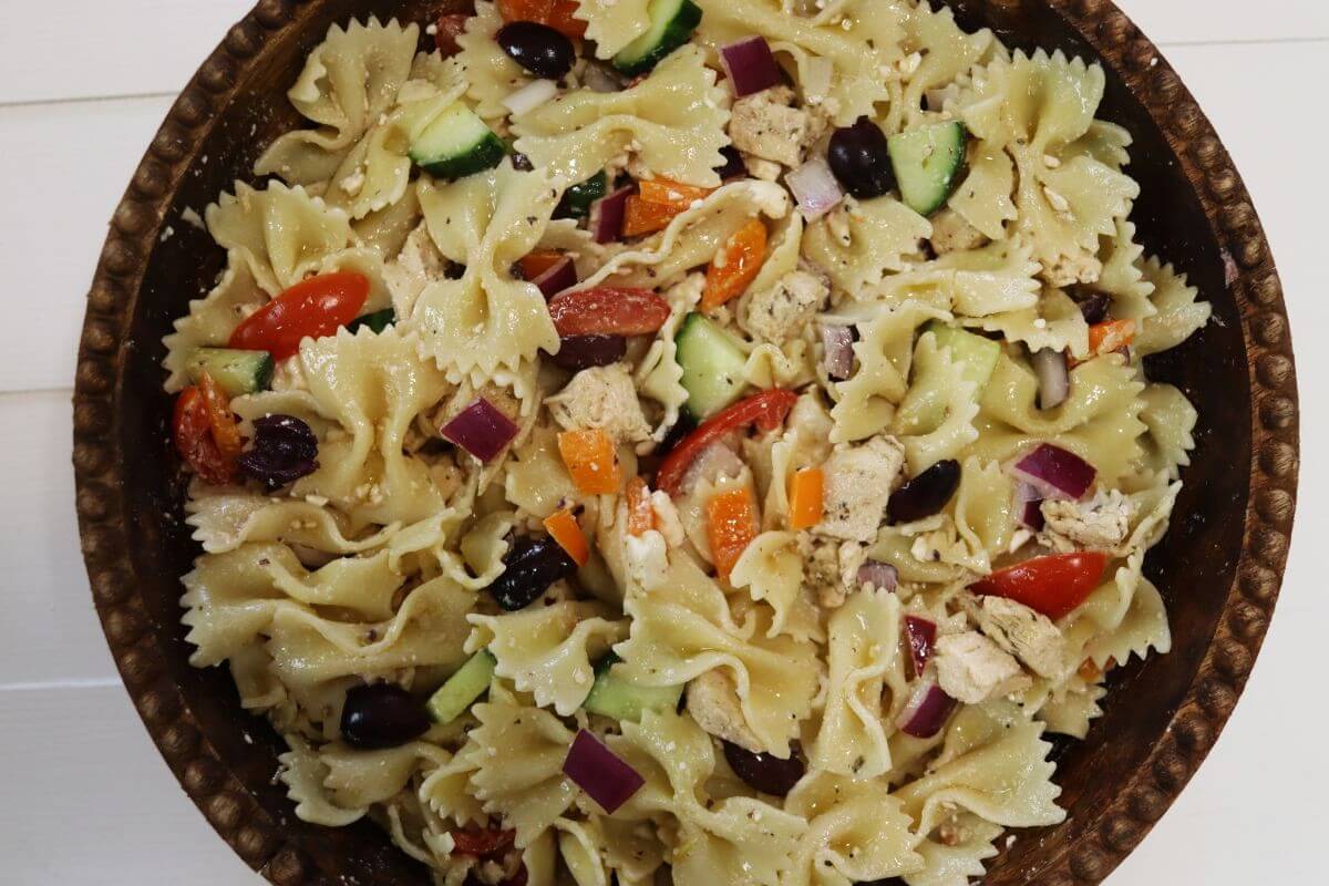Bowl of greek chicken pasta salad with farfalle, vegetables, olives, and feta.