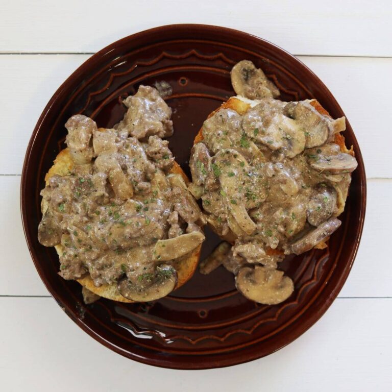 Two open-faced sandwiches topped with mushroom stroganoff mixture on a brown plate.