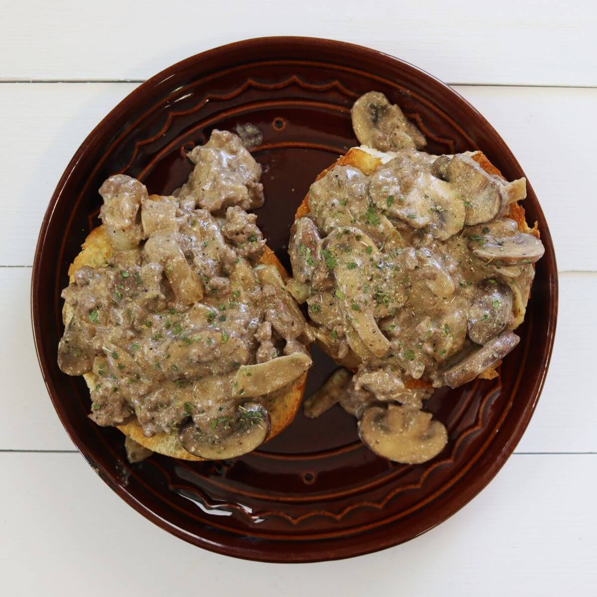 Two open-faced sandwiches topped with mushroom stroganoff mixture on a brown plate.