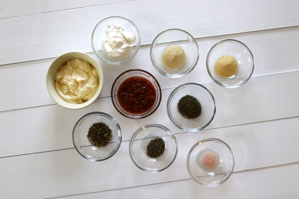 Small bowls of mayonnaise, sour cream, salsa, herbs, spices, and salt on white table.