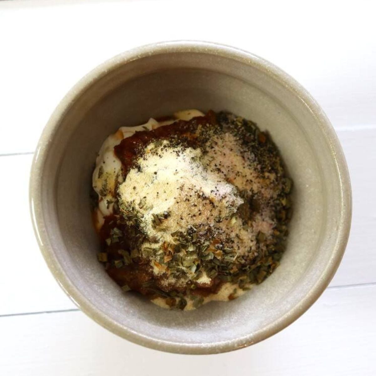 Mayonnaise, sour cream, salsa, herbs, and spices in a bowl on white table.