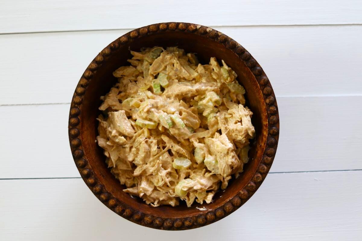 Chicken salad with celery in a brown bowl on a white wooden surface.