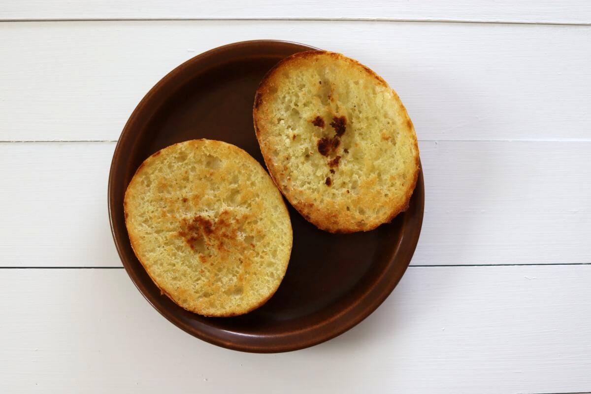 Toasted sandwich bun halves on a brown plate on a white wooden surface.