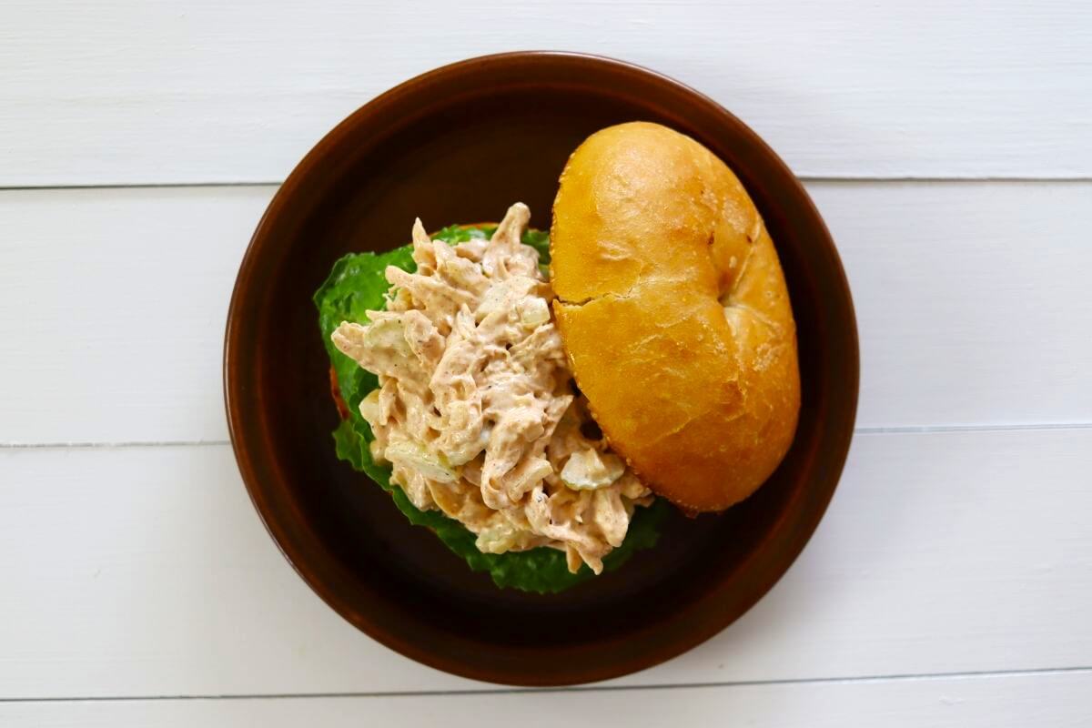 Chicken salad with celery on lettuce in a bun on a brown plate.
