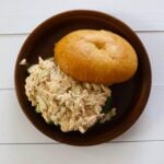 Chicken salad with celery on lettuce in a bun on a brown plate on a white wooden surface.