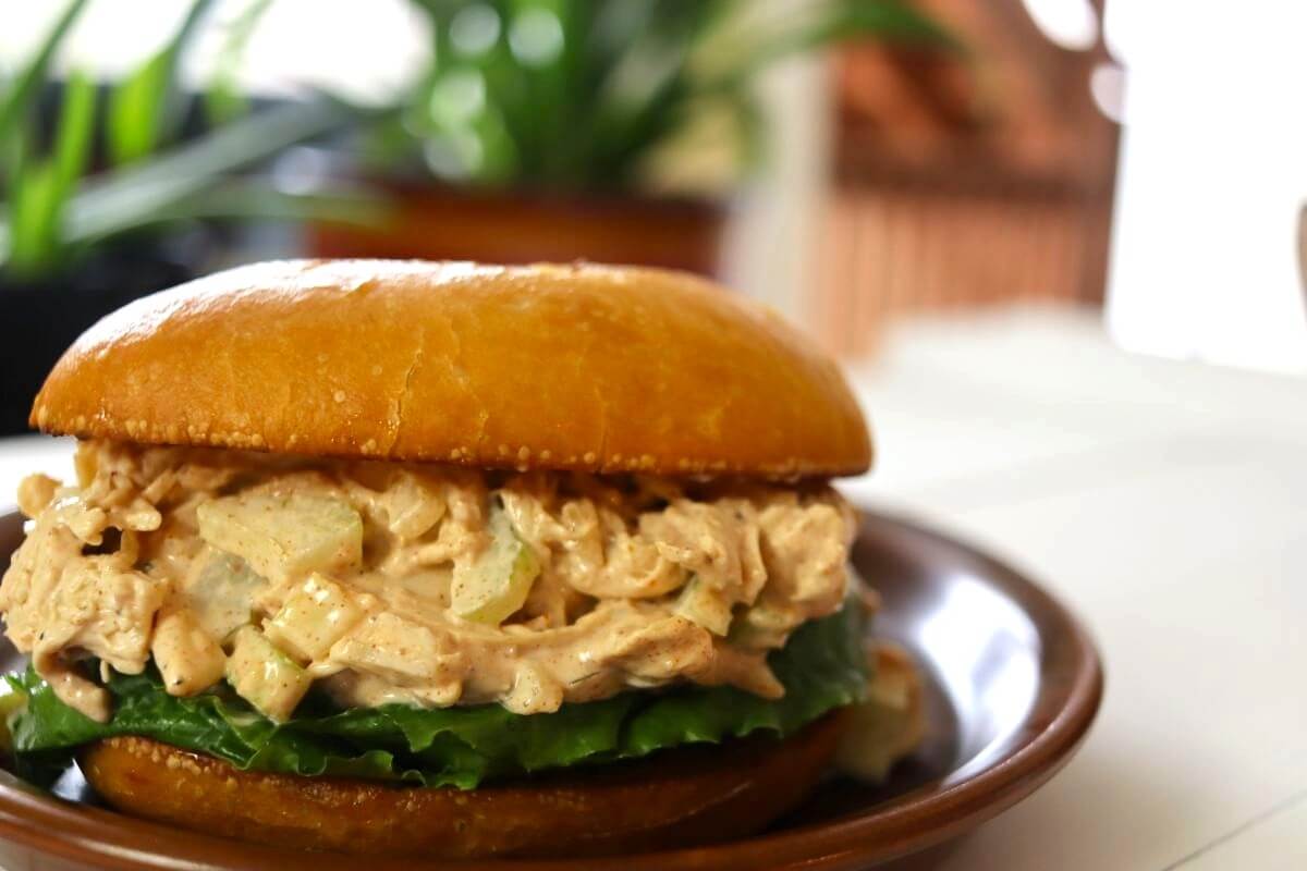 Chicken salad sandwich with lettuce on a bun, served on a brown plate.