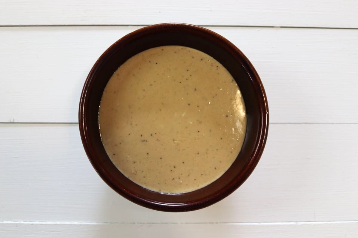Small bowl of balsamic mayonnaise dressing with visible pepper on white wooden surface.
