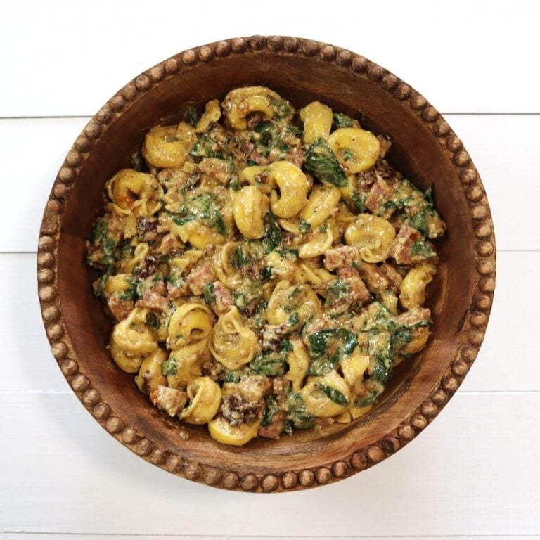 Cheese tortellini pasta salad with spinach, salami pieces, and sun-dried tomatoes in bowl.