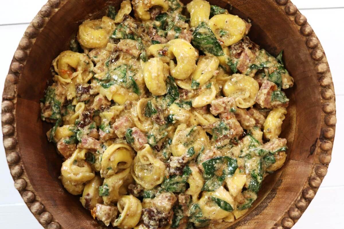 Tuscan tortellini pasta salad with spinach, salami, and sun-dried tomatoes in a wooden bowl.