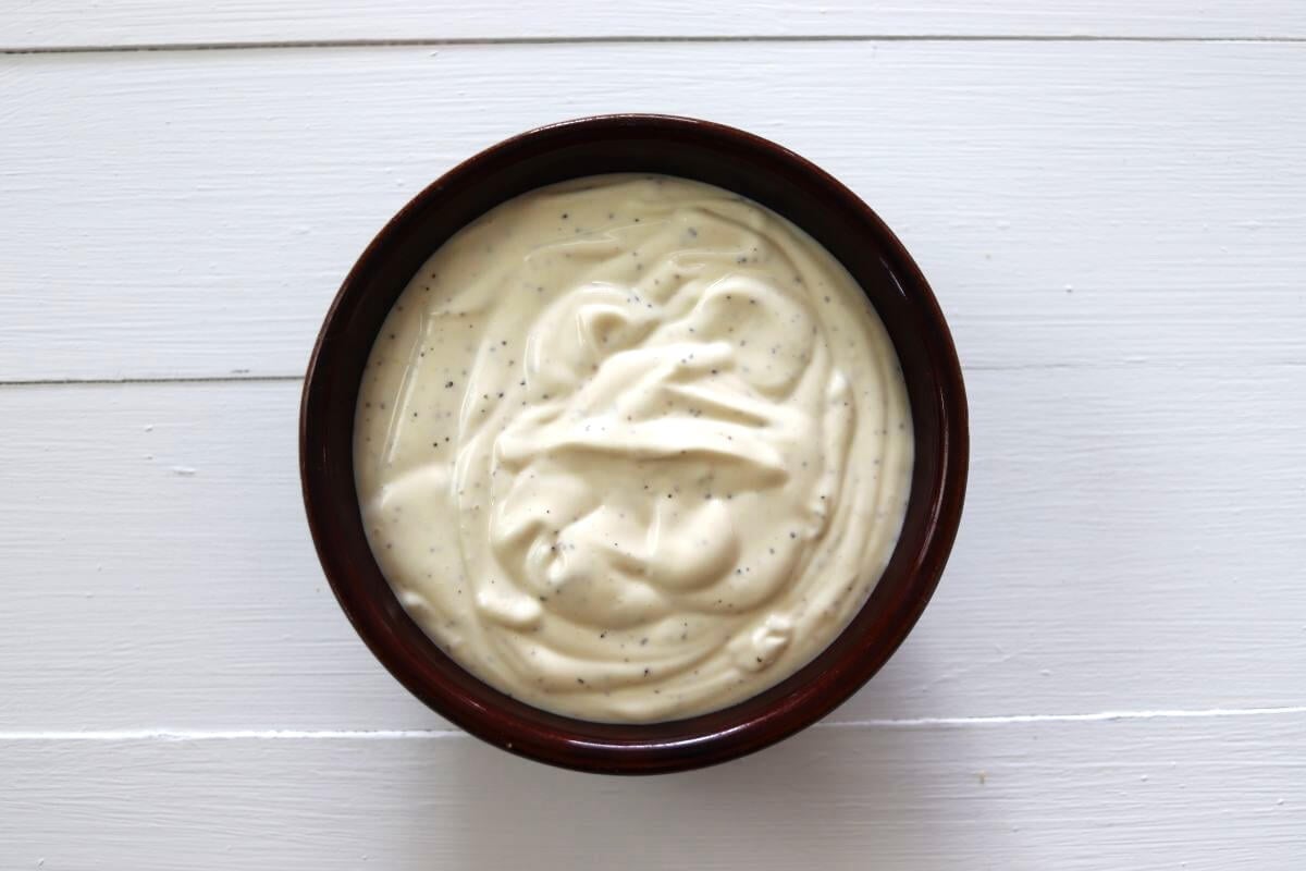 Mayonnaise mixture with visible spices in a small bowl on a white surface.