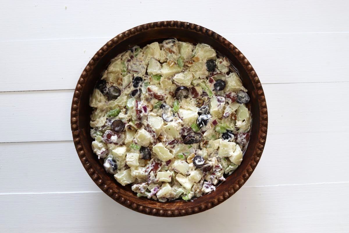 Chopped potatoes mixed with grapes, apple, celery, walnuts, and dressing in a serving bowl.