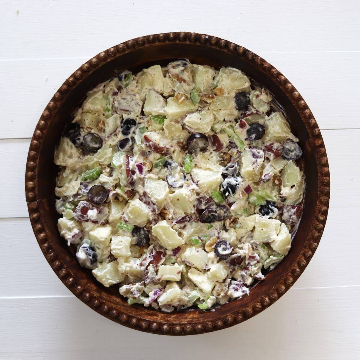 Potato salad with grapes, apple pieces, celery, walnuts, and red onion in a brown bowl.
