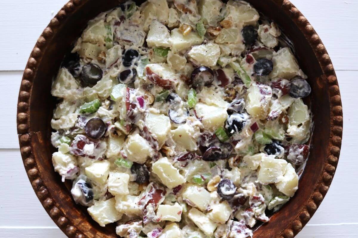 Waldorf potato salad with red potatoes, grapes, apple, celery, and walnuts in a bowl.