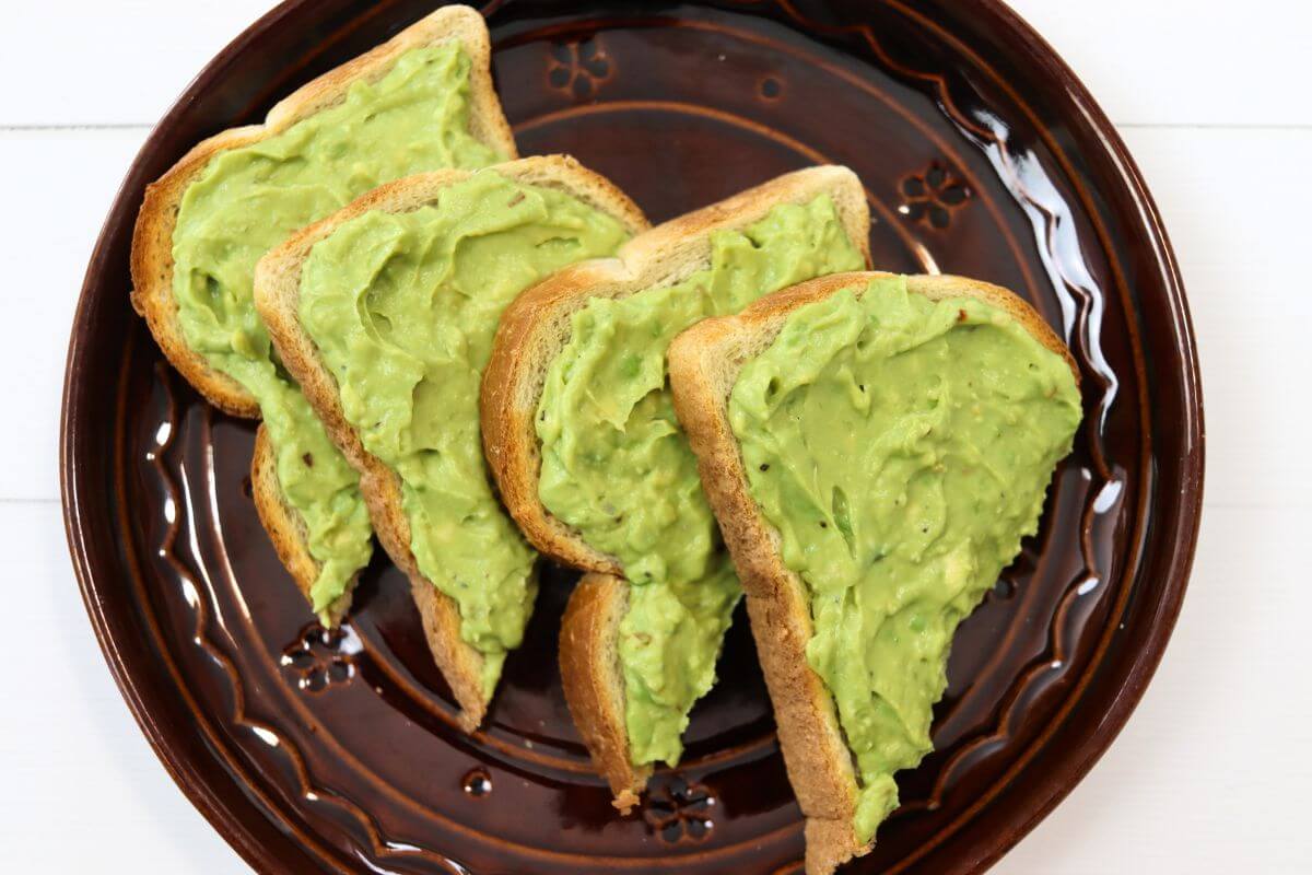 Four slices of avocado toast arranged on a brown ceramic plate.