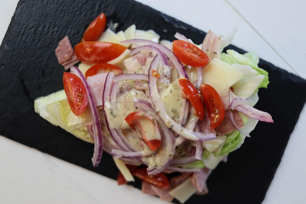 Chopped Italian grinder wedge salad with ham, salami, provolone, onion, tomatoes, and dressing on iceberg.