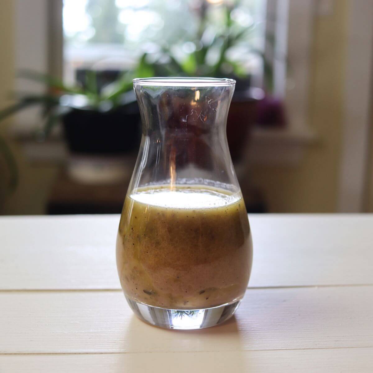 Glass carafe filled with creamy submarine dressing on a white table.