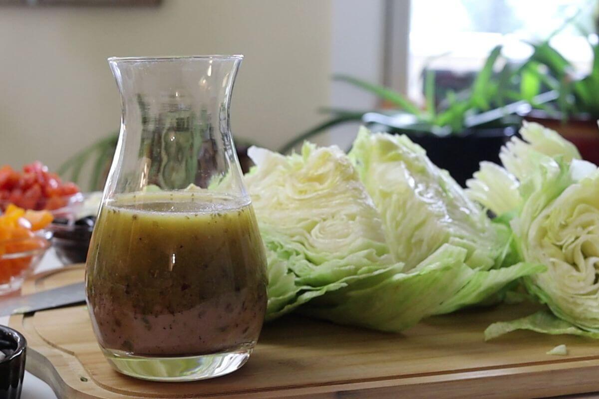 Glass carafe of vinaigrette with separated oil and vinegar beside iceberg lettuce wedges.