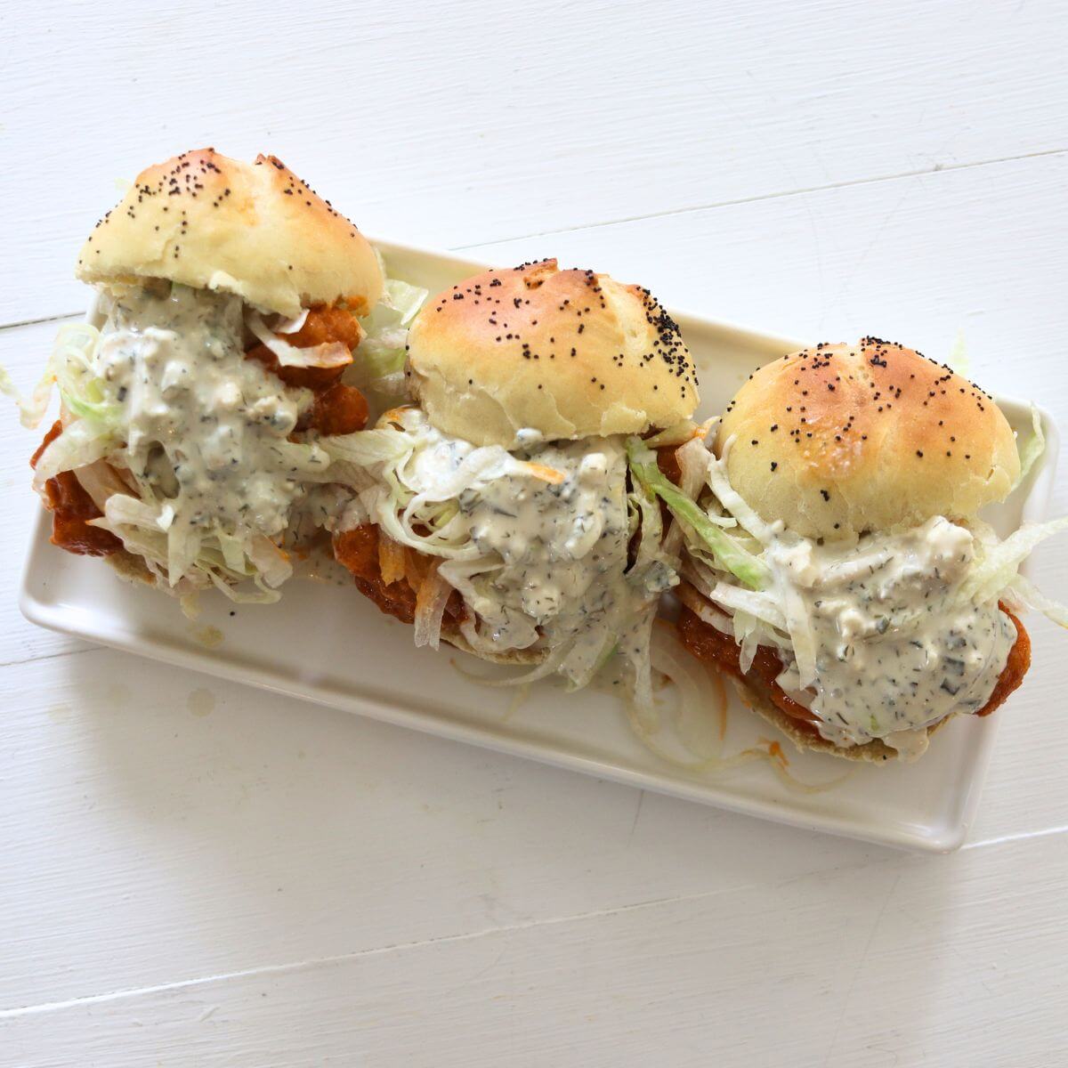 Crispy buffalo chicken sliders with lettuce and dressing on poppy seed slider buns.
