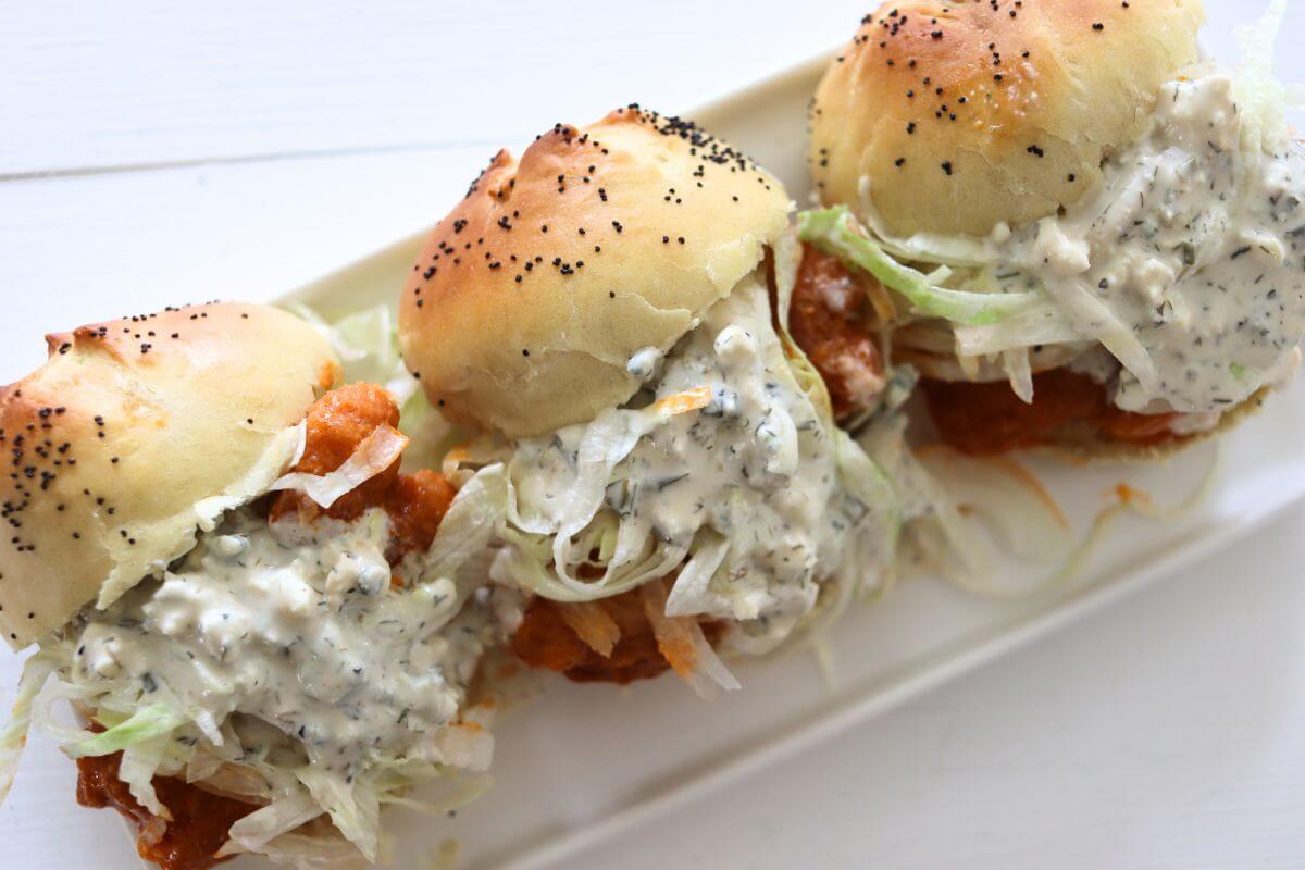Three buffalo chicken sliders with shredded lettuce and dressing on poppy seed buns.