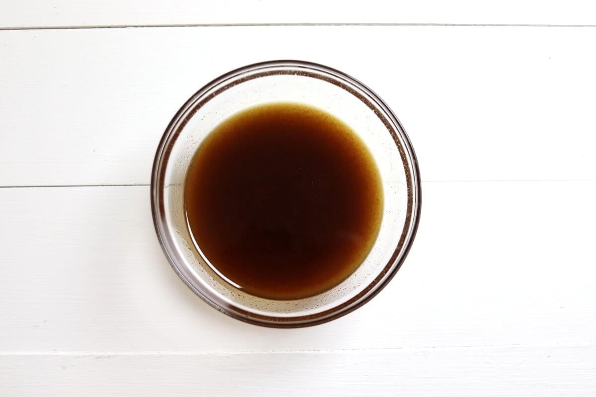 Small glass bowl with honey mixture on white wooden surface.