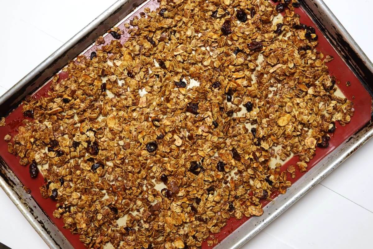 Baked oat mixture with almonds and cranberries on silicone-lined baking sheet.