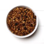 White bowl filled with baked granola containing oats almonds and cranberries.