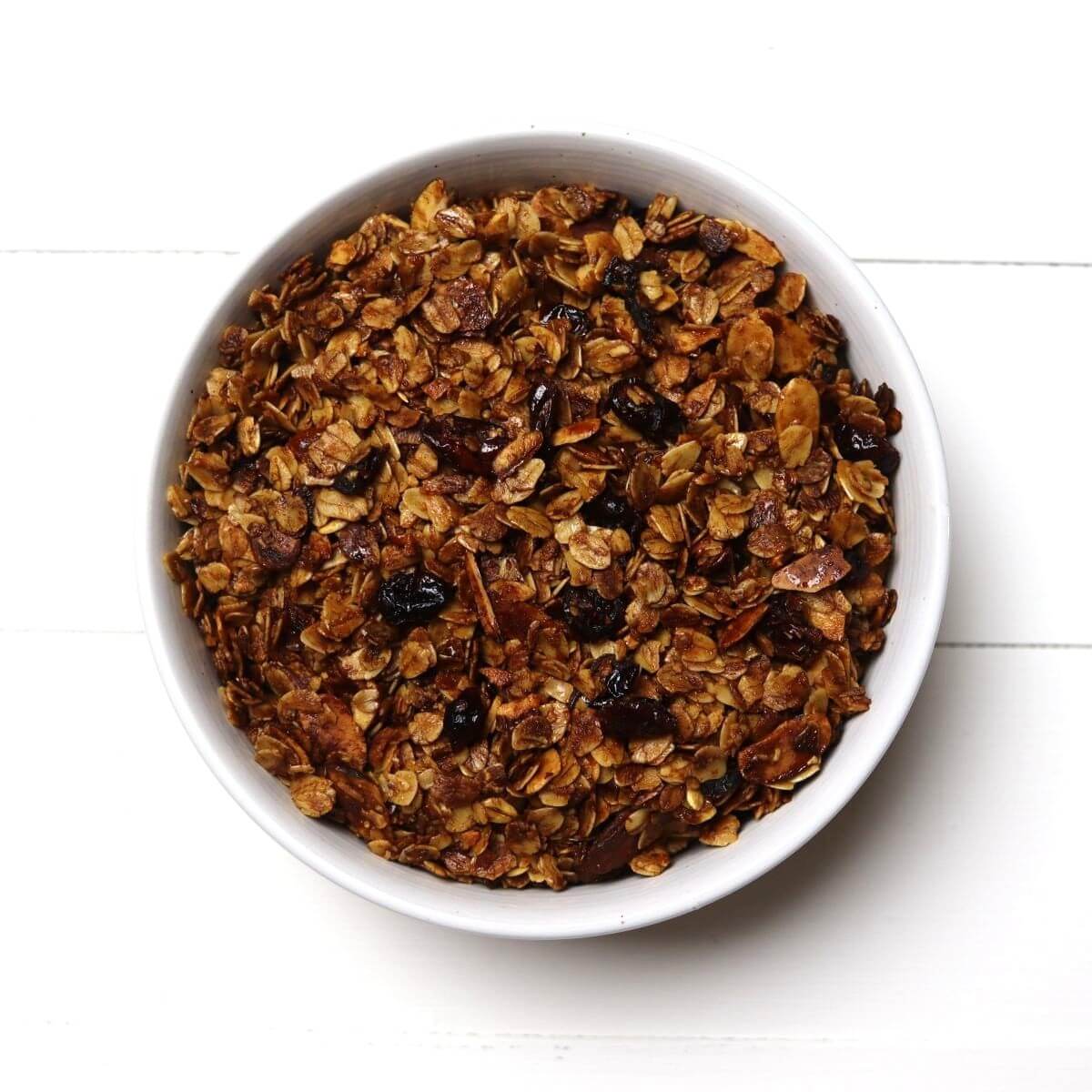 White bowl filled with baked granola containing oats almonds and cranberries.