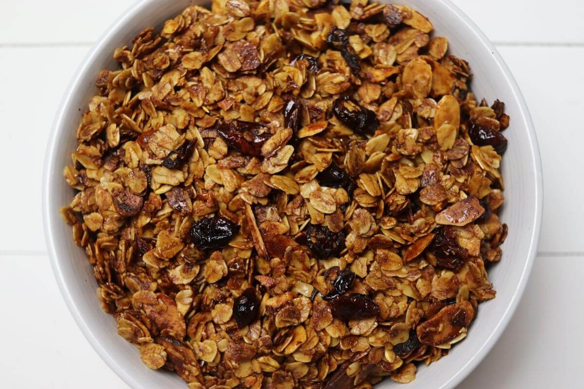 White bowl filled with homemade honey granola with oats almonds and cranberries.