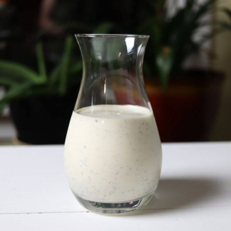 Glass carafe filled with farmhouse ranch dressing from scratch on a white surface.