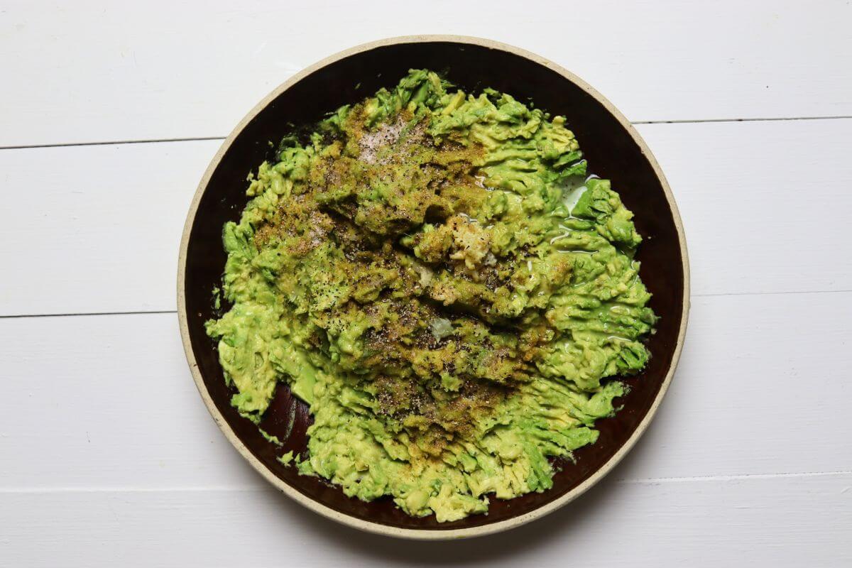Mashed avocado in a bowl topped with lime juice, garlic, and spices.