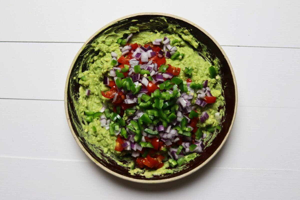 Mashed avocado in a bowl topped with diced tomatoes, red onion, and jalapeño.